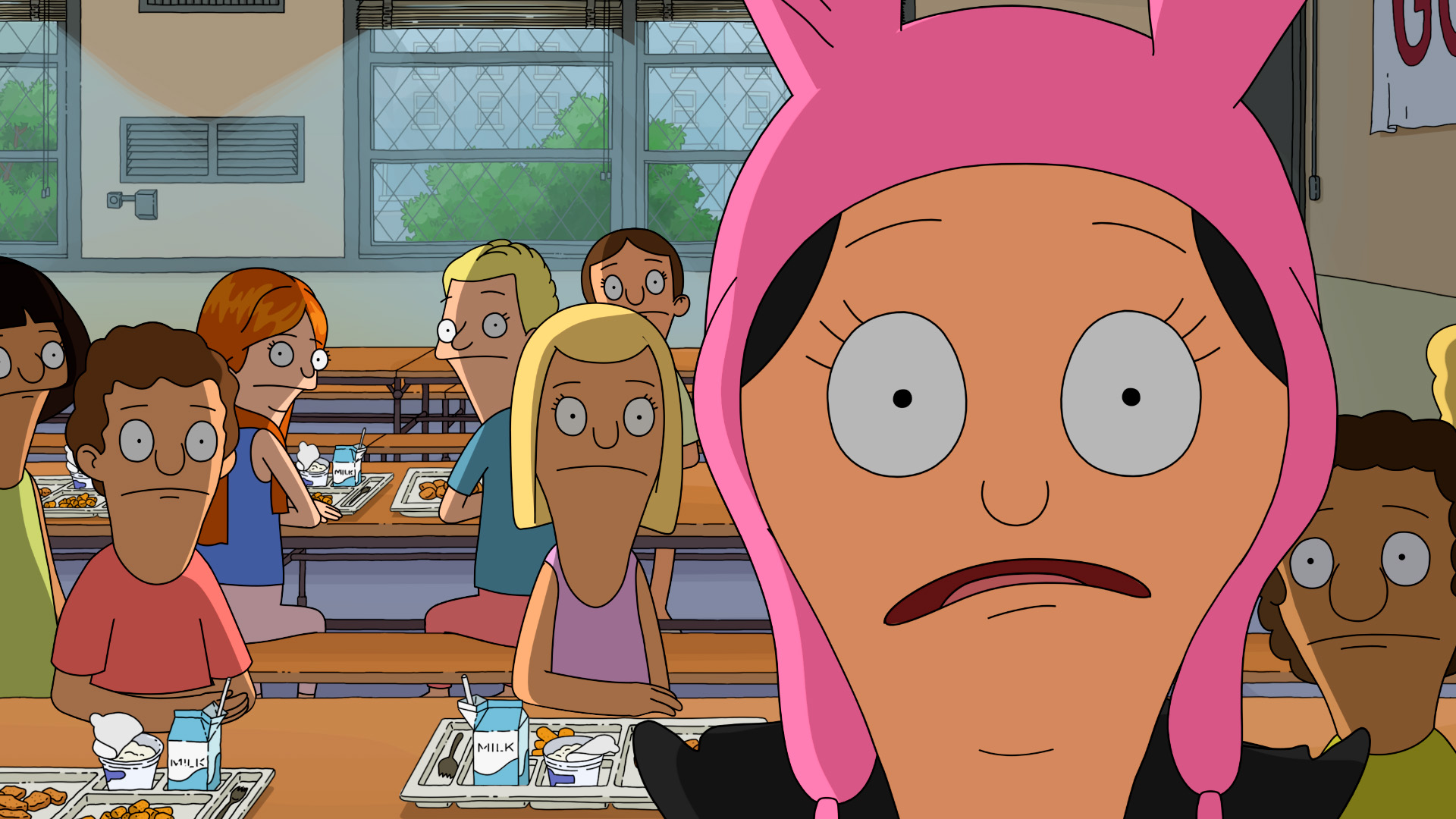 A close up of Louise looking shocked in her school cafeteria while kids eat their lunch and watch her from the background.